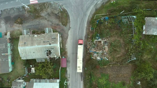 Ukrayna 'daki Rus saldırısından kaynaklanan yıkık dökük bir şehirden insani yardım taşıyan bir kamyon. Mavi ve sarı römorklu kırmızı kamyon. Şehir ve yollar yıkıldı. 4K hava aracı