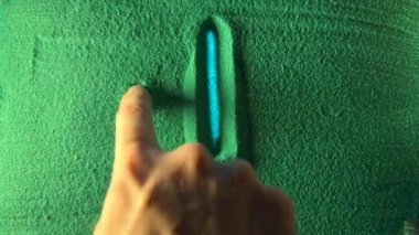 Hand drawing the arrow to down in the Green Sand. Male hand writes the arrow to down on the green sand with blue backlight. Top view 4k resolution