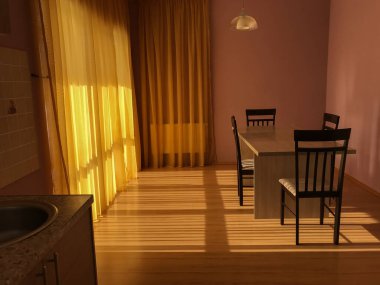 Batan güneş ışınları, temiz ve minimalist olan sarı mutfağa doğru parıldıyor. Çizgilerin ve şekillerin basitliği