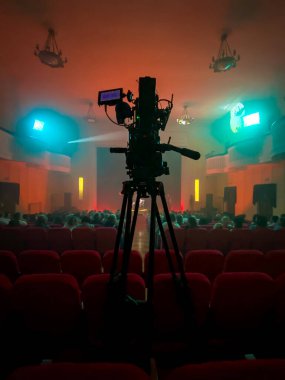 Konser salonunun ortasında tripodun üzerinde duran bir film kamerası etkinliği bekliyor.