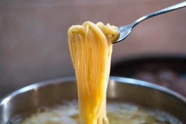 Ocakta tencereye konmuş spagetti. Sıcak suda spagetti. Tencereden çatalla al ve pişmesini izle. Spagetti evde pişirmeye hazır..