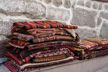 Taş bir duvarın önünde katlanmış bir halı yığını. Ankara Şatosu 'nda otantik Türk halıları satıldı.