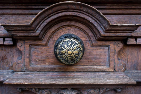 Closeup of a fragment of an old (ancient, medieval) wooden entrance door to the castle, palace, cathedral with elements of wood carving and metallic round golden handles in the shape of a flolower.