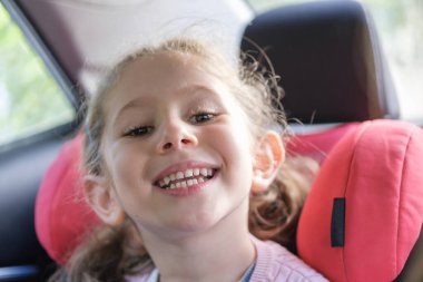 Ulaşım, güvenlik, çocukluk yolculuğu ve insanların konsepti. Arabada oturan mutlu küçük kız. Küçük mutlu beyaz kız çocuğu büyük bir gülümsemeyle ön dişlerini gösteriyor. seçici Odaklanma dişleri.