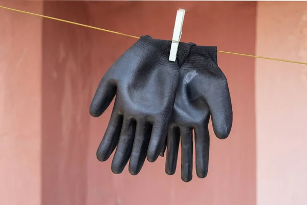 Hanging, black rubber gloves on the clothes line. Red Wall Background. Selective Focus Gloves