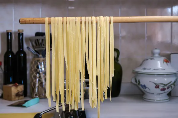 Mutfak tezgahında makarna makinesiyle tagliatelle hazırlıyorum. Tahtada asılı duruyor. Yakın plan..