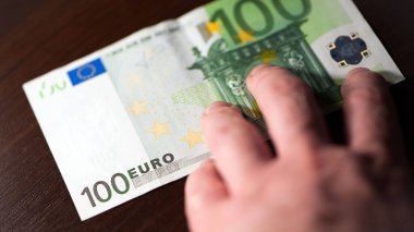 Kahverengi Tahta Masa 'da Erkek Eli Tutuşu 100 Avro banknotu. Kağıt para, para, nakit. Finans, ödeme, ticaret, finansal işlemler, refah kavramları. yakın plan