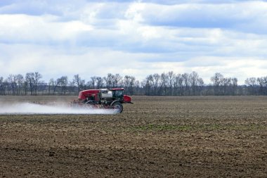 Bulutlu bir günde tarlayı sulayan sulama sistemi olan bir traktör. Tarım makineleri. Mevsimlik iş. Traktör toprağı gübreler. Sahada at sürüyor.