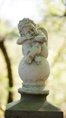 Parktaki melek heykeli. Kanatlı küçük çocuk. Spring Park 'taki aşk tanrısı heykeli. Tasarım için biblo, mermer üzgün bir melek topun üzerinde oturuyor. Bulanık doğal arkaplan