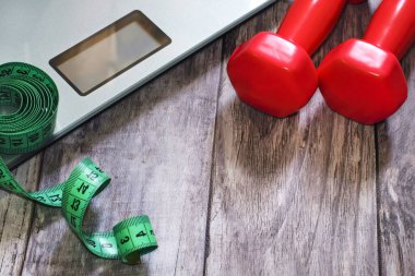 Elektronik ölçekler. Spor temalı forma sağlıklı yaşam tarzı dambıllar ağırlık spor malzemeleri. Fitness teması, ahşap arka planda spor aksesuarları. Evde beden eğitimi ve evde kalma kavramı