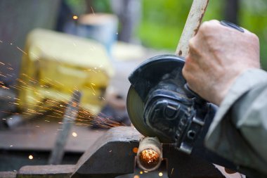 Açı öğütücüyle çeliği kesen ağır endüstri işçisi. Paslı bir boruyu kesiyorum. Parçalanıyor. Yakın plan. Eski pipo ve öğütücüyle çalışmak. Bir ustanın elleri, profesyonel. Sıcak metal kıvılcımları uçuşuyor