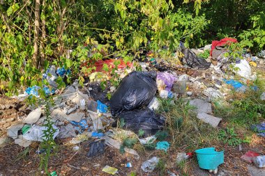 Kyiv, Ukrayna, 19.08.2024. Ormanda çöp yığınları, doğaya rastgele atılanlar. Pis kokulu hurda, plastik torba ve şişeler, doğanın kirli otlarının içindeki çöpler. Ekoloji. Yazı