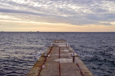 Beton iskele, deniz manzarası, ufuk, bulutlardaki gökyüzü. Boş bir beton iskele konsepti hayal et, tatil, yaz, denize yolculuk. Eski iskele. Gün doğumunda dalgalı ve bulutlu bir yüzey görüntüsü