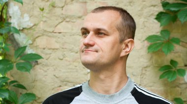 Genç Avrupalı. Erkek portresi. Adam tuğla duvarın önünde duruyor. fotoğraf, gülümseme, düşünceli, şaşırmış, kızgın, duygular, duygular. Açık tenli, sakallı. 30-40 yaşlarında bir adam. yakın plan