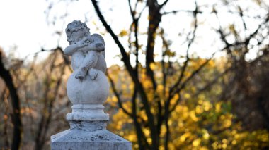 Parktaki melek heykeli. Kanatlı küçük çocuk. Autumn Park 'taki aşk tanrısı heykeli. Tasarım için biblo, mermer üzgün bir melek topun üzerinde oturuyor. Bulanık doğal arkaplan