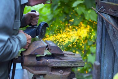 Yaşlı adam çalışıyor. Metal bir boruyu kesmek. Kıvılcım. Boru mengeneye sıkışmış. Adamın elleri öğütücü tutuyor. Eski demir mengene, paslı boru. Metalle çalışan elektrikli bir alet. Bulgarca, disk öğütücü
