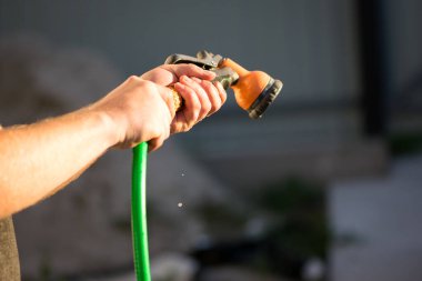 Çim sulama hortumu elinde. Fıskiye, sulama suyu, arka bahçeyi sulama. Yeşil hortum, turuncu sprey, erkek eli, arka bahçe, bahçıvan, yakın plan.