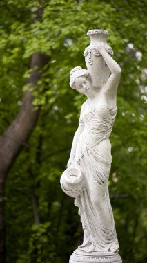 Bahar parkında bir kızın heykeli. Şehir parkında yarı çıplak bir Yunan ya da İtalyan Rönesans kadınının vazosu olan eski bir heykel. Yaz bahçesinde. Yakın plan. Bir sürahi su.