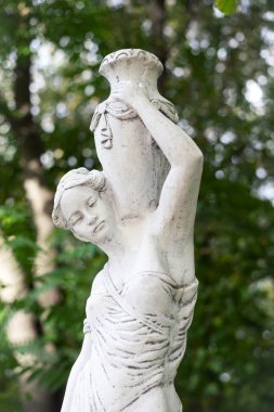 Bahar parkında bir kızın heykeli. Şehir parkında yarı çıplak bir Yunan ya da İtalyan Rönesans kadınının vazosu olan eski bir heykel. Yaz bahçesinde. Yakın plan. Bir sürahi su.