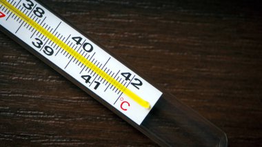 Karanlık bir arkaplanda cam termometre, sıcaklığı ölçmek, termometre izole, yakın plan, ahşap bir masa üzerinde. Hastalık konsepti, yüksek ateş. Metin için boşluk