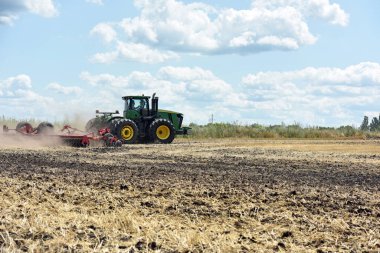 Tarlada traktör, tarlada saban süren bir traktör. Tarlada çalışan büyük yeşil traktör, toprak hazırlığı, hasat, ticaret, tarım
