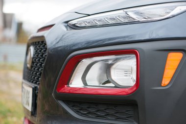 Modern prestijli arabanın ön farları yakın plan. Güzel bir arabanın farları. Koyu gri, kırmızı kenarlı. Ön tarafın bir kısmı, araba tanınmaz halde. Bir spor arabanın yön göstergeleri