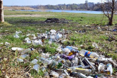 Kyiv, Ukrayna, 02.04.2017. Nehir kıyısındaki çöp yığınları, doğaya rastgele atılanlar. Plastik torba ve şişeler, kirli çimenlerdeki çöpler, doğa manzarası. İnsan kirliliği ekolojisi. Yazı