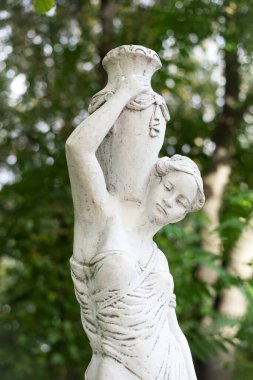 Bahar parkında bir kızın heykeli. Şehir parkında yarı çıplak bir Yunan ya da İtalyan Rönesans kadınının vazosu olan eski bir heykel. Yaz bahçesinde. Bir sürahi su.