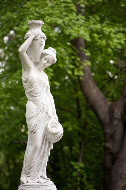 Bahar parkında bir kızın heykeli. Şehir parkında yarı çıplak bir Yunan ya da İtalyan Rönesans kadınının vazosu olan eski bir heykel. Yaz bahçesinde. Bir sürahi su.