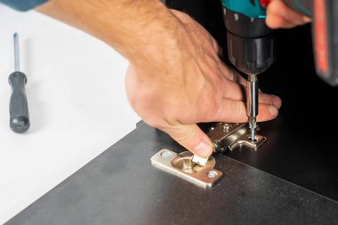 Mobilya montajı sırasında ön kapıya menteşe kurulumu. Bulanık arkaplanı olan vidalara seçmeli odaklan ve metin için boşluğu kopyala.