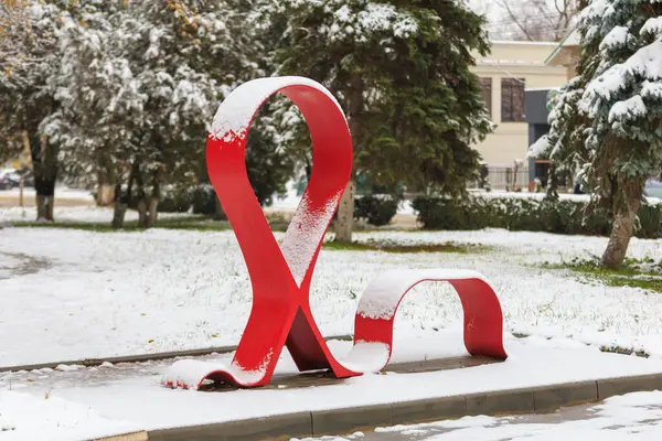 エイズとの戦いを象徴する象徴的な赤い金属リボンの白い雪 選択的なフォーカスを持つ背景 — ストック写真