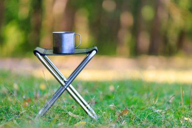 Yürüyüş ya da kamp gezisi için katlanır sandalyede metal bir kupa. Seçici odak ve kopyalama alanı olan arkaplan