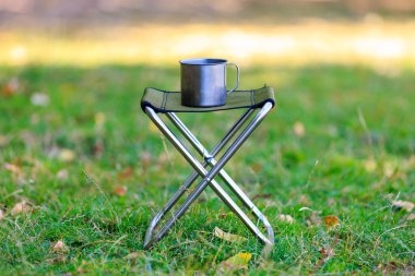 Yürüyüş ya da kamp gezisi için katlanır sandalyede metal bir kupa. Seçici odak ve kopyalama alanı olan arkaplan