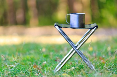 Yürüyüş ya da kamp gezisi için katlanır sandalyede metal bir kupa. Seçici odak ve kopyalama alanı olan arkaplan