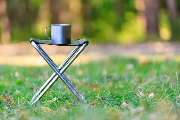 A metal mug on a folding chair for a hike or camping trip. Background with selective focus and copy space