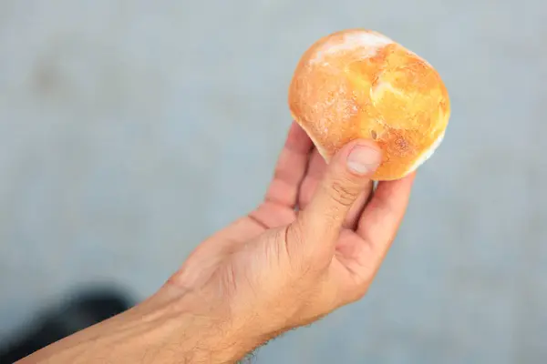 A man's hand holds a round bun, snack and fast food concept. Selective focus on hands with blurred background and copy space for text.