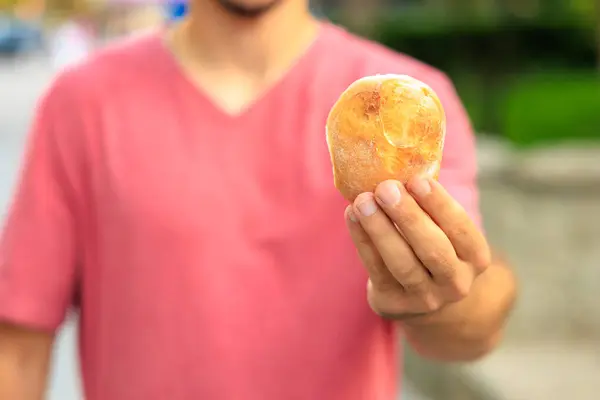 A man\'s hand holds a round bun, snack and fast food concept. Selective focus on hands with blurred background and copy space for text.
