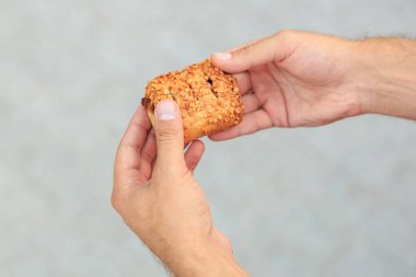 Bir adamın eli reçelli, abur cuburlu ve fast food konseptli tatlı bir hamur işi tutuyor. Bulanık arkaplan ve metin için kopyalama alanı olan ellere seçici odak.