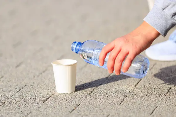 A woman's hand pours water into a paper cup. The concept of giving the dog water in the heat. Caring for animals. Background with selective focus and copy space for text