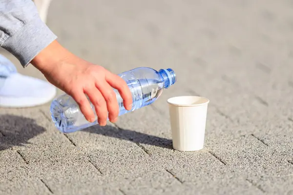 A woman\'s hand pours water into a paper cup. The concept of giving the dog water in the heat. Caring for animals. Background with selective focus and copy space for text