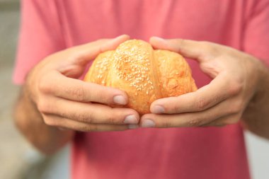 Adamın elinde kruvasan, aperatif ve fast food konsepti var. Bulanık arkaplan ve metin için kopyalama alanı olan ellere seçici odak.