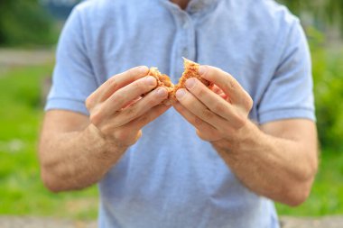 Bir adamın eli reçelli, abur cuburlu ve fast food konseptli tatlı bir hamur işi tutar. Bulanık arkaplan ve metin için kopyalama alanı olan ellere seçici odak.