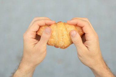 Bir adamın elinde kruvasan, aperatif ve fast food konsepti vardır. Bulanık arkaplan ve metin için kopyalama alanı olan ellere seçici odak.