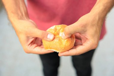 Bir adamın eli yuvarlak bir çörek, atıştırmalık ve fast food konseptini tutar. Bulanık arkaplan ve metin için kopyalama alanı olan ellere seçici odak.