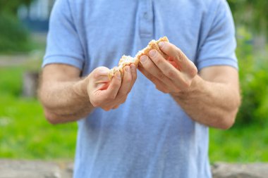 Adamın elinde mini ekmek, atıştırmalık ve fast food konsepti var. Bulanık arkaplan ve metin için kopyalama alanı olan ellere seçici odak.