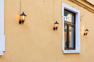 Sokak manzaralı bir pencere ve duvardan sarkan bir lamba. Aydınlatma armatürü yanıyor ve pencere açık.