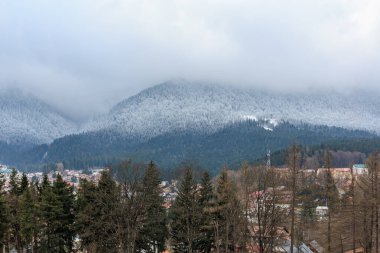 Karla kaplı dağlar ve sis, kışın kırsal bir kasabaya tepeden bakıyor..