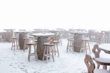 Snow-covered outdoor bar furniture in a misty atmosphere. clipart