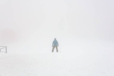 Karlı yamaçta yoğun siste tek başına kayakçı.