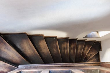 Güneş ışığıyla aydınlatılmış, ahşap sarmal merdiven. Gölgesi ve taş duvarları var..